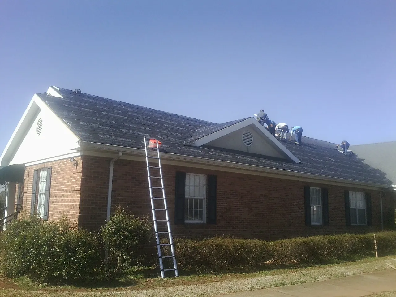 Crew tearing shingles off a brick ranch roof with a ladder set — Emergency Roof Repair work by our crew in Nutley