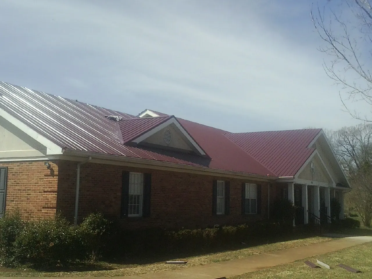 Red metal roof with gabled entries on a long brick building, from a Hail Damage Roof Repair job in Nutley