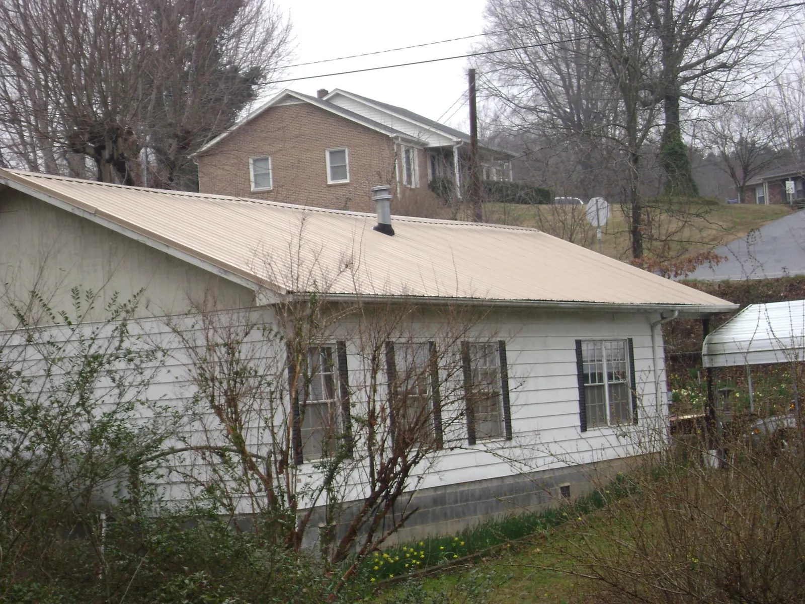 Tan metal roof on a white sided house set into a hillside — Commercial Roofing by Roofing Brothers in Nutley